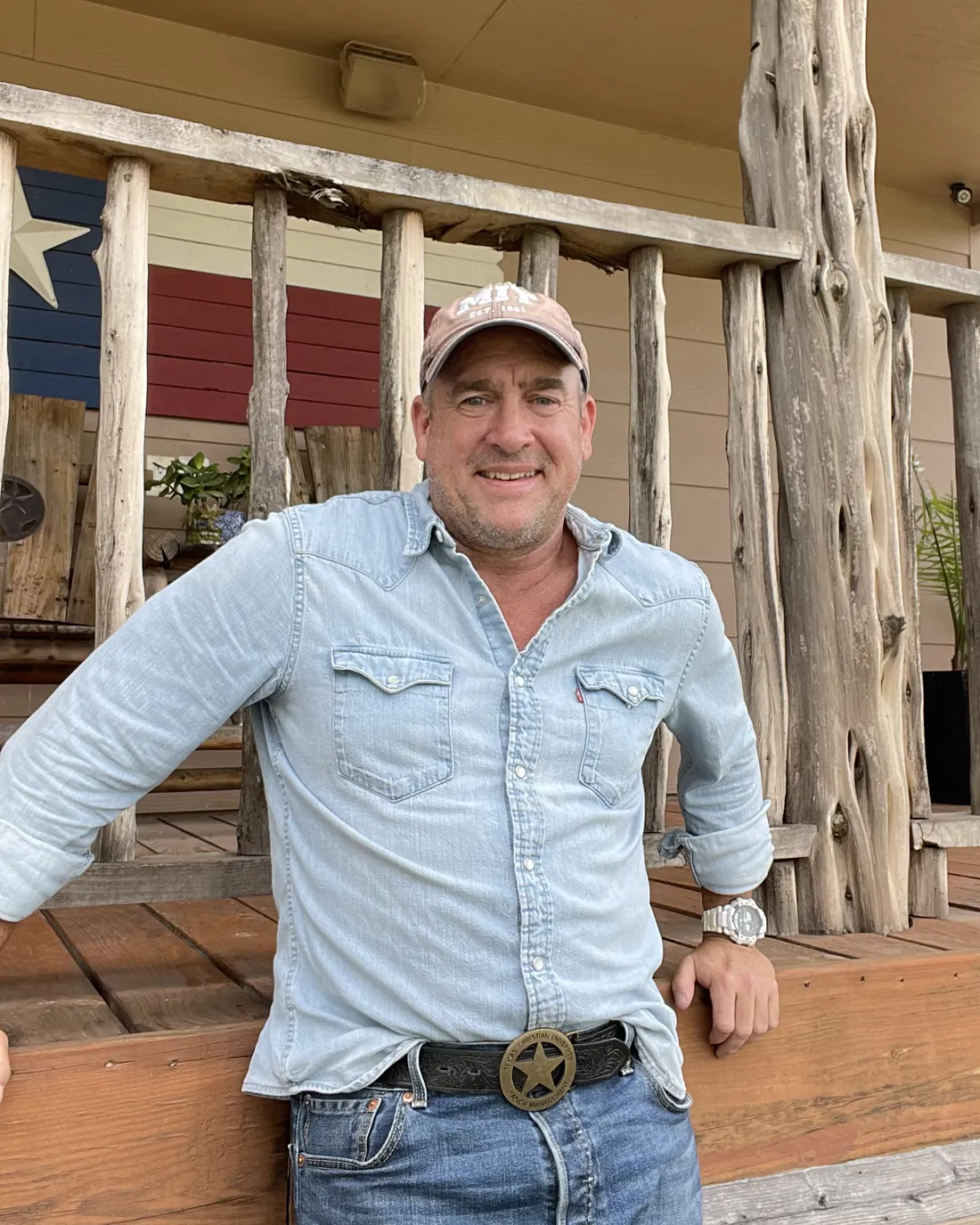 Tres Curtis, owner of Roof Shield Texas, on a porch beside a Texas flag
